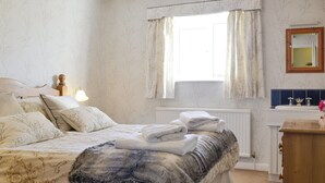 Un dormitorio con cama, mesita de noche, ventana con cortinas, radiador y espejo.