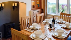 Un coin repas avec une table en bois, dressée pour quatre personnes, entourée de chaises, et offrant une vue sur la verdure à l’extérieur.