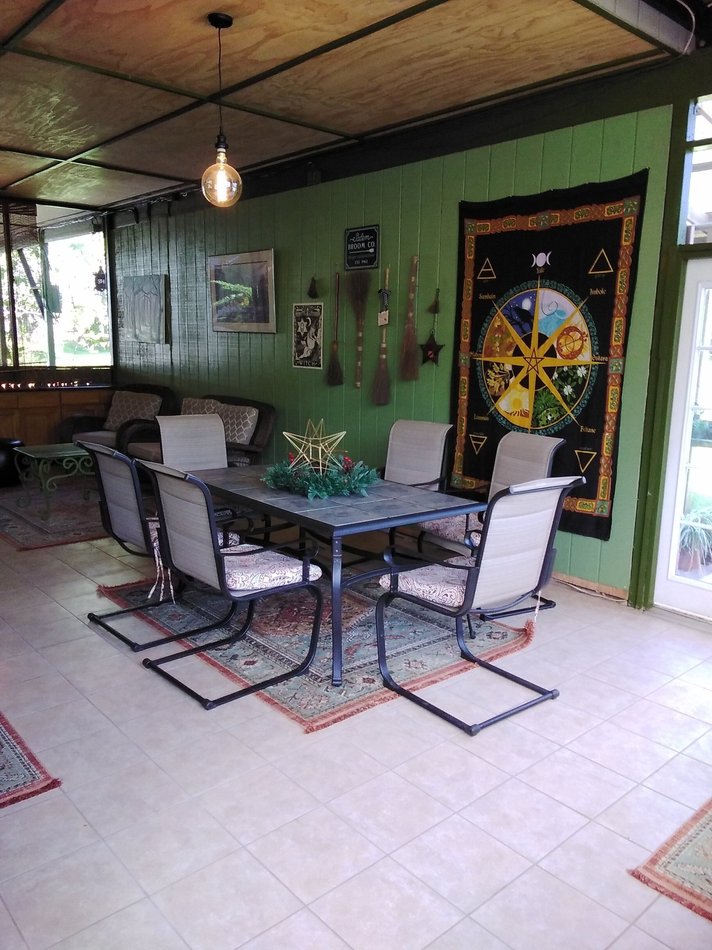 A dining area with a table and chairs, a hanging light fixture, and a wall tapestry.