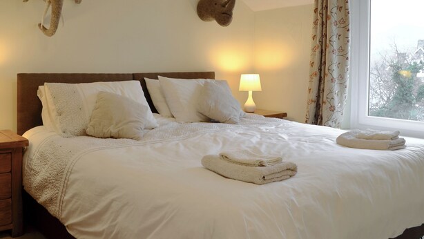 A neatly made bed with white linens and pillows, a bedside lamp, and two mounted animal heads on the wall. - 3 bedroom accommodation in Keswick (Keswick)