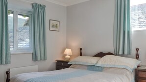 A bedroom with a bed, a nightstand, a lamp, a framed picture on the wall, and a window with curtains.