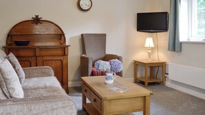A living room with a wooden cabinet, a sofa, a chair, a coffee table, a lamp, a clock, and a television.