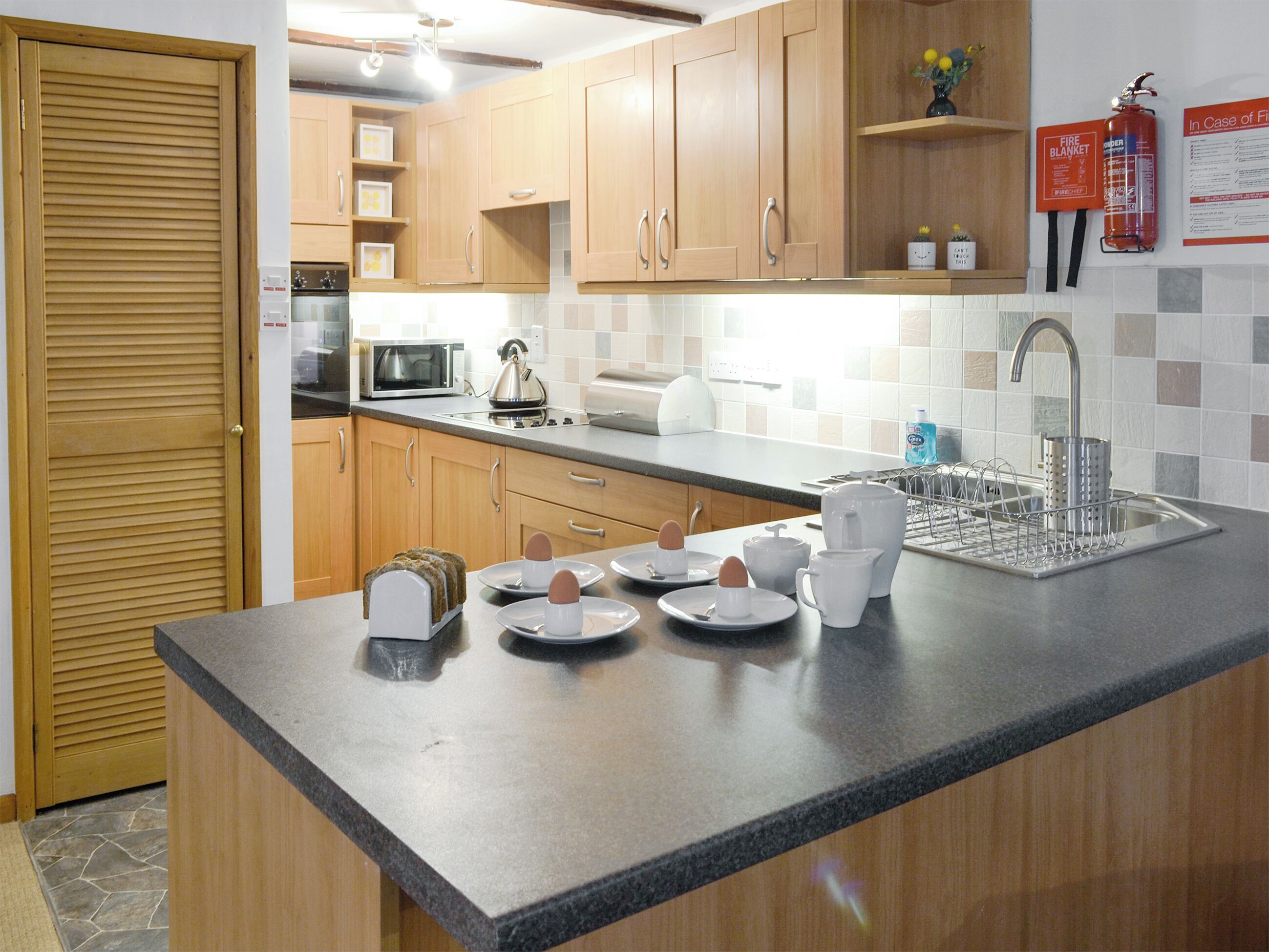 A modern kitchen with wooden cabinets, a microwave, a kettle, and a sink with a dish rack.