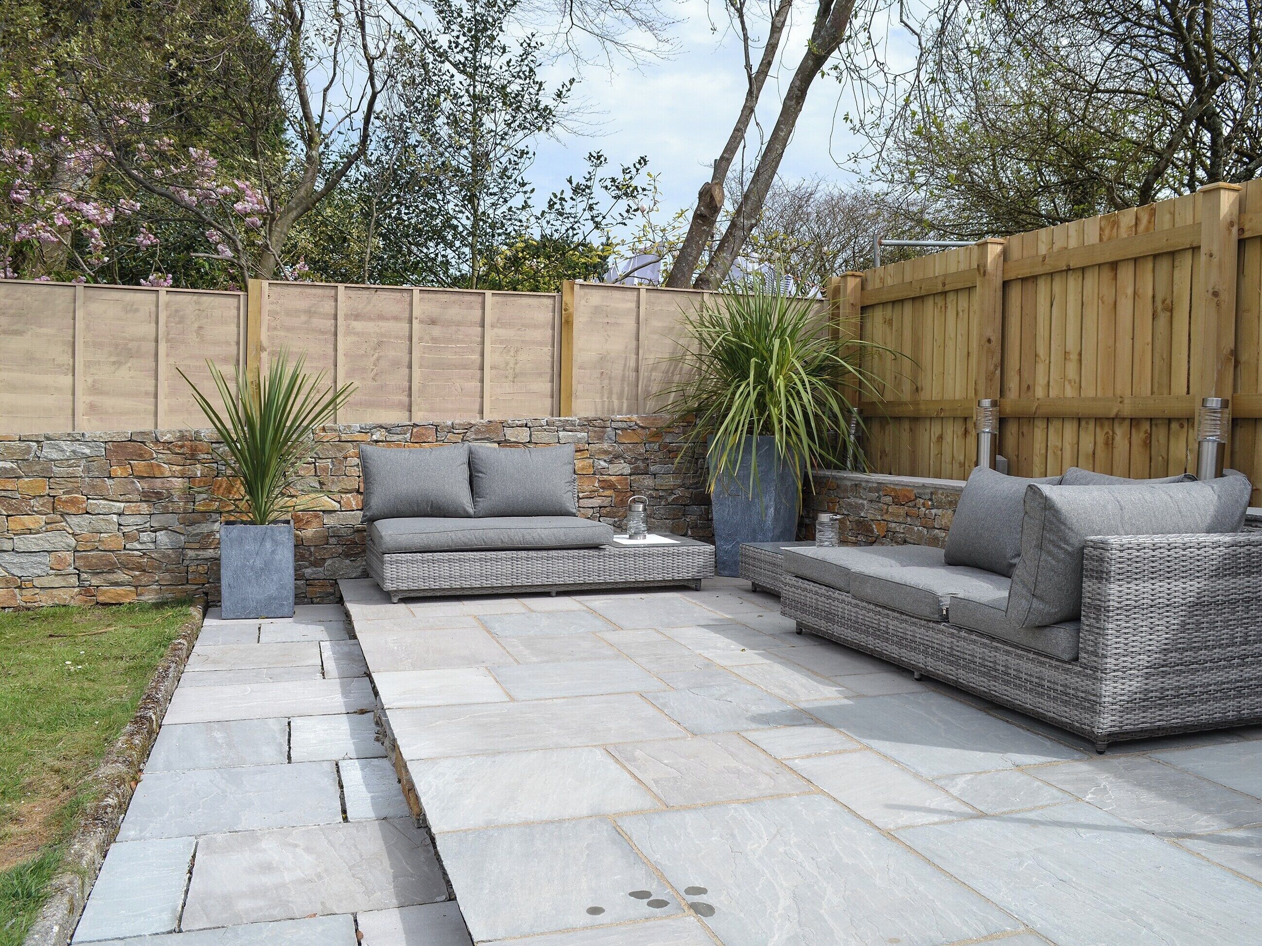 A patio with stone flooring, wicker furniture, and a stone wall.