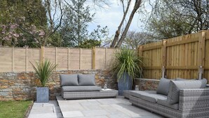 A patio with stone flooring, wicker furniture, and a stone wall. - 5 bedroom accommodation in Newquay (Newquay)