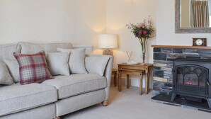A living room with a sofa, a small table with a lamp, a vase with flowers, and a fireplace. - 5 bedroom accommodation in Newquay (Newquay)