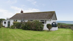 Una casa de un piso con techo inclinado, un pequeño jardín delantero y vista al mar.