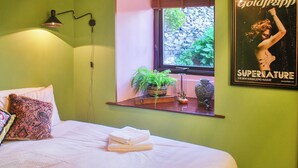 A bedroom with a bed, a nightstand, a window with a view of rocks and greenery, a wall-mounted lamp, and a framed poster on the wall. - A break at Bandrake Barn offers rest and relaxation. (Oxen Park, near Ulverston)