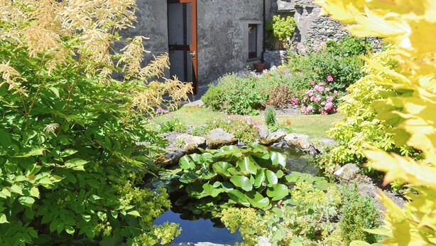 A stone building with a wooden door, surrounded by a garden with a small pond and various plants. - A break at Bandrake Barn offers rest and relaxation. (Oxen Park, near Ulverston)