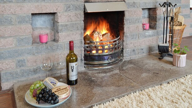 Una chimenea de piedra con fuego, una botella de vino y un plato de uvas.