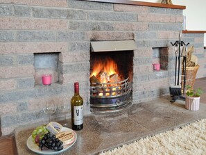 Une cheminée en pierre avec un feu de bois, une bouteille de vin et une assiette de raisins.