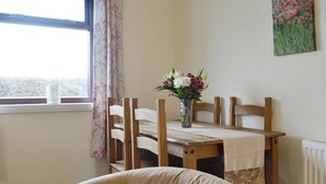 A dining area with a wooden table, chairs, a vase with flowers, a window with curtains, and a radiator.