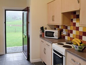 A kitchen with a microwave, stove, and a bowl of fruit on the counter.