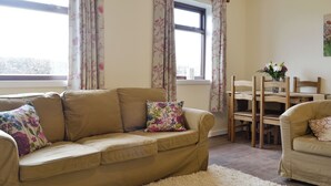 A living room with a beige sofa, a white shag rug, and a wooden dining table with chairs.