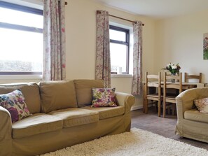 Ein Wohnzimmer mit einem beigefarbenen Sofa, einem weißen Shaggy-Teppich und einem Holzesstisch mit Stühlen.