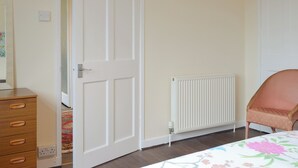 Un dormitorio con un aparador de madera, un radiador y una silla.