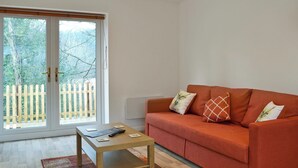 A living room with a sofa, a small table, and a sliding glass door leading to a balcony with a wooden fence. - 2 bedroom accommodation in Godstone (Godstone)