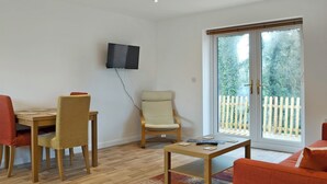 A living room with a television mounted on the wall, a dining table with chairs, a sofa, and a sliding glass door leading to a balcony. - 2 bedroom accommodation in Godstone (Godstone)