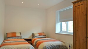 A bedroom with two beds, a wooden wardrobe, a window with a blind, and a thermostat on the wall. - 2 bedroom accommodation in Godstone (Godstone)
