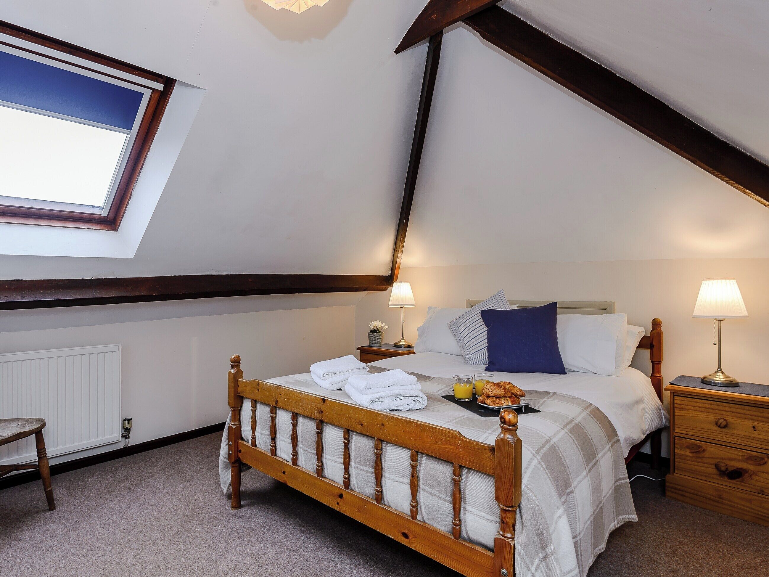 Une chambre à coucher avec un lit en bois, deux tables de chevet, une commode, une fenêtre donnant sur un paysage agréable et un puits de lumière.