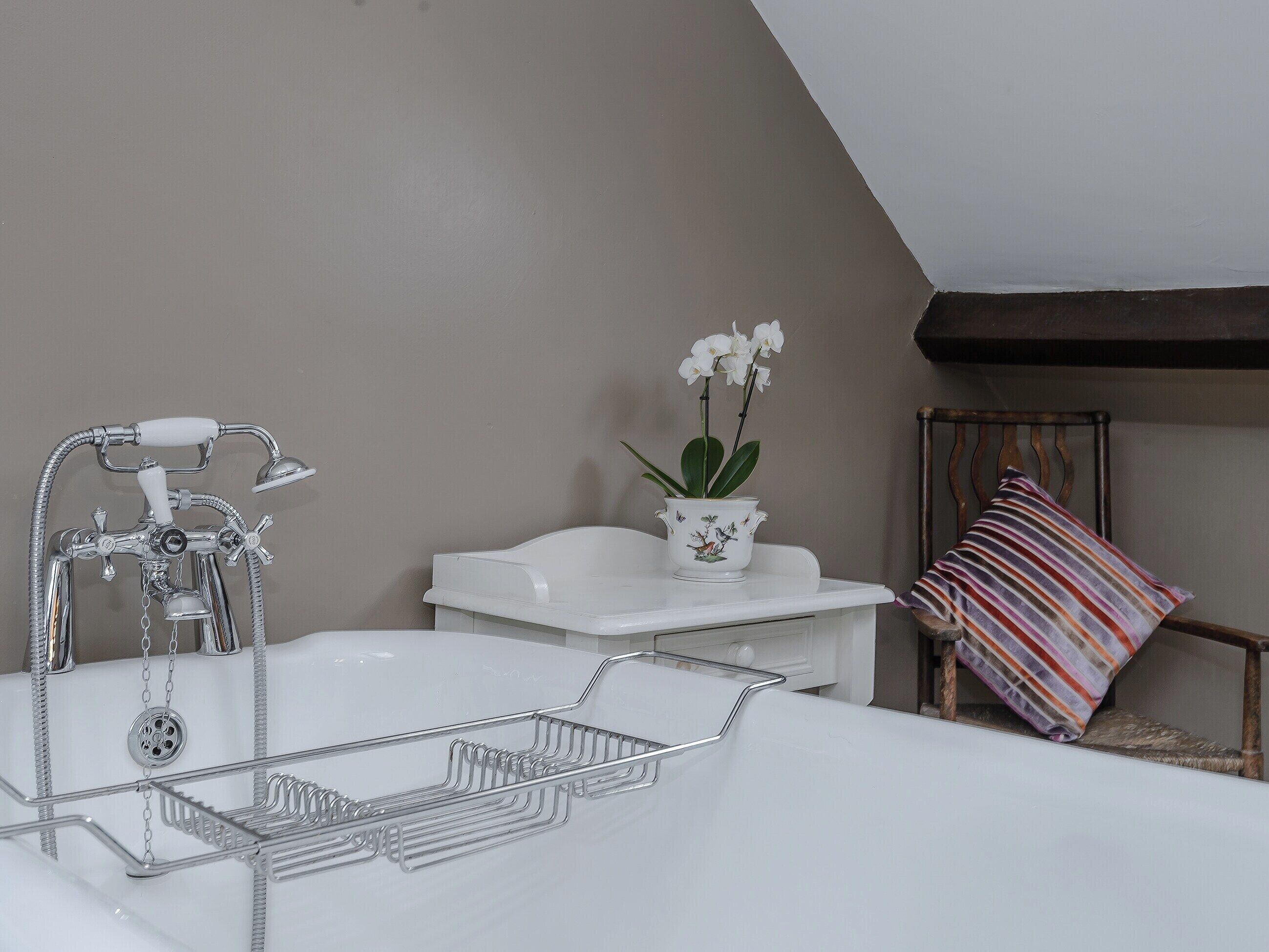 A bathroom with a bathtub, a shower, and a sink. There is a white vase with flowers on the sink counter.