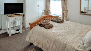 A bedroom with a bed, a TV on a stand, a wardrobe, a window with curtains, and a mirror on the wall. - 2 bedroom accommodation in Wells-next-the-Sea (Wells-next-the-Sea)