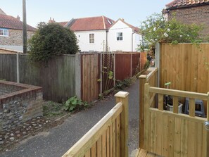 Un étroit sentier mène à une porte en bois, bordée d’un mur de pierre et d’une clôture en bois.