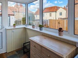 Een kamer met een erker, met uitzicht op een woonwijk, met een houten bankje en potplanten.
