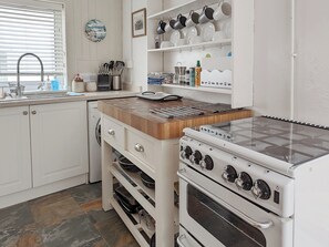Une cuisine avec des armoires blanches, un plan de travail en bois, une cuisinière et un évier.