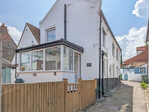 Un bâtiment blanc avec une clôture en bois, une petite construction attenante dotée d’une fenêtre et une enseigne indiquant « Trinity Cottage ».