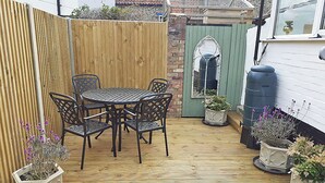 Eine Holzterrasse mit rundem Tisch und Stühlen, umgeben von Topfpflanzen.