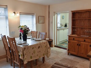 A dining area with a table set for four, wooden chairs, a vase with flowers, and a kitchen visible through an open door. - 2 bedroom accommodation in Wells-next-the-Sea (Wells-next-the-Sea)
