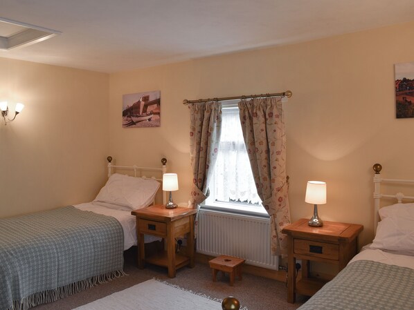 A bedroom with two single beds, bedside tables with lamps, a window with floral curtains, and a radiator. - 2 bedroom accommodation in Wells-next-the-Sea (Wells-next-the-Sea)