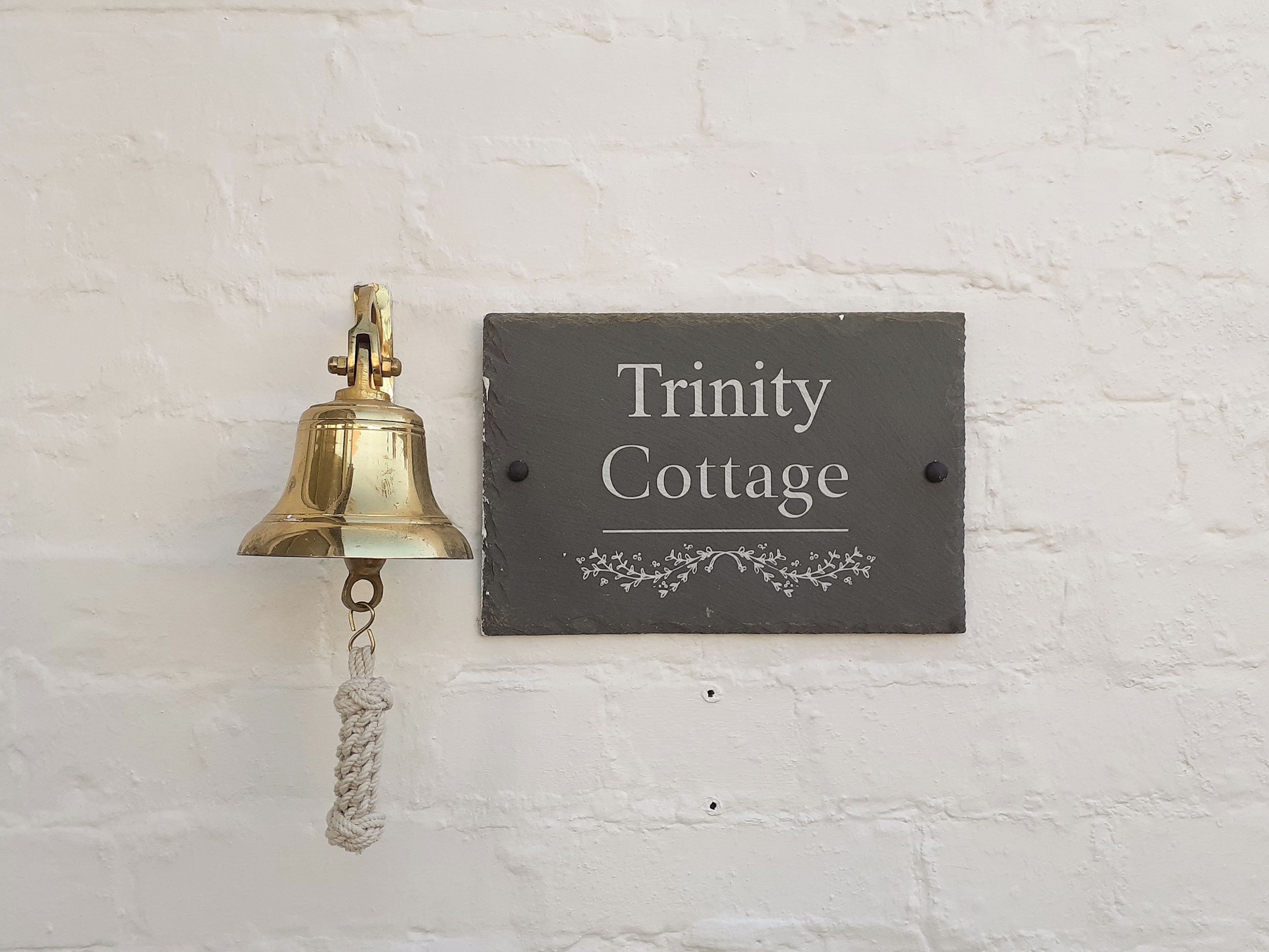 A brass bell and a sign reading "Trinity Cottage" mounted on a white wall.