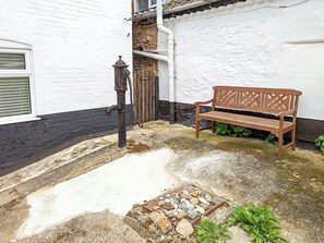 Een stenen bank, een waterput en een witte muur met een zwarte plint.