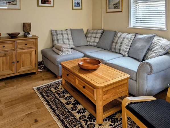 Un salon chaleureux avec un canapé gris, une table d’appoint en bois et un tapis à motifs.