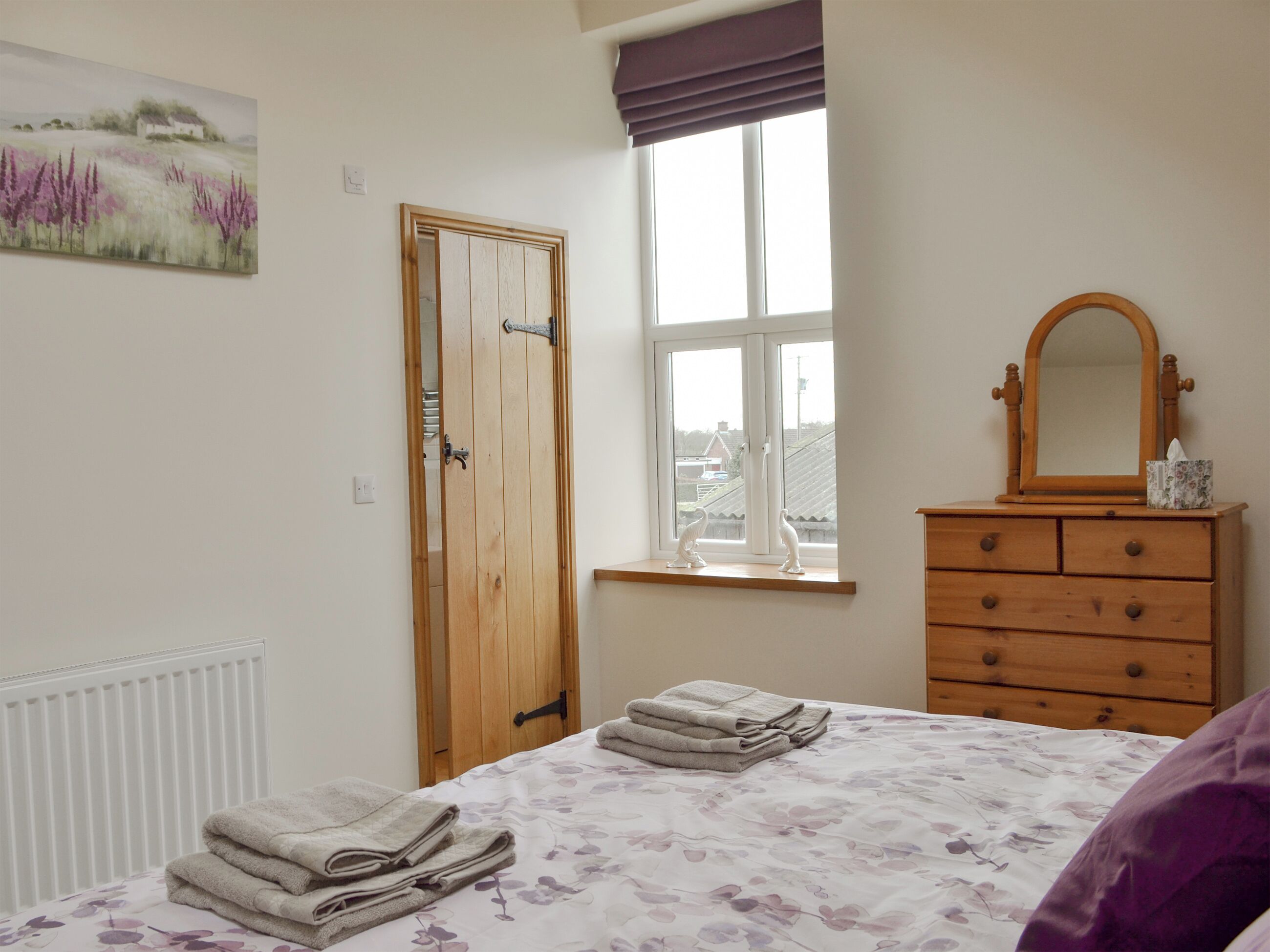 Une chambre à coucher avec un lit, une commode, une fenêtre donnant sur un beau paysage, une porte et un tableau accroché au mur.