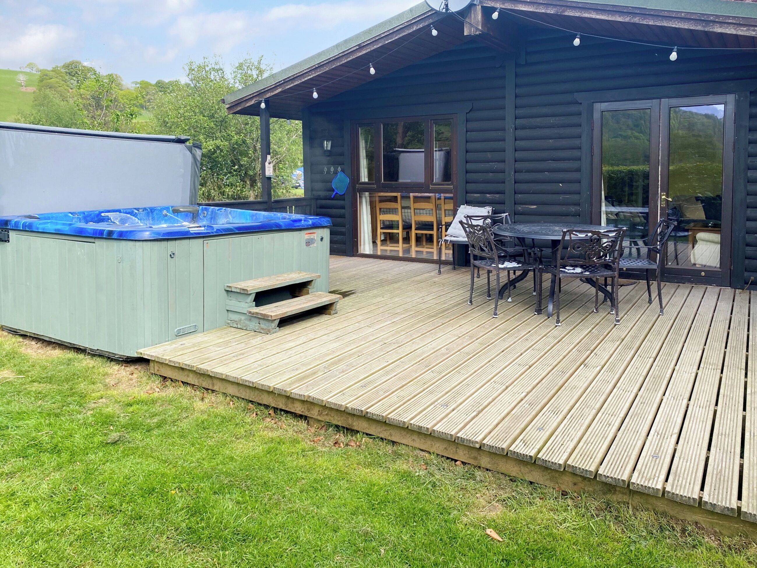 Eine Holzterrasse mit Whirlpool, Sitzgelegenheiten im Freien und einer Glasdoor zu einer überdachten Patio.