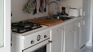 A kitchen with white cabinets, a stove, an oven, and a countertop. - Villa Tre Palme Pagghiari (vulcano)