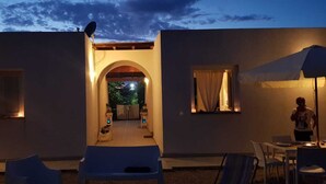 A modern building with a covered outdoor seating area, a central archway, and a patio with a table and chairs. - Villa Tre Palme Pagghiari (vulcano)
