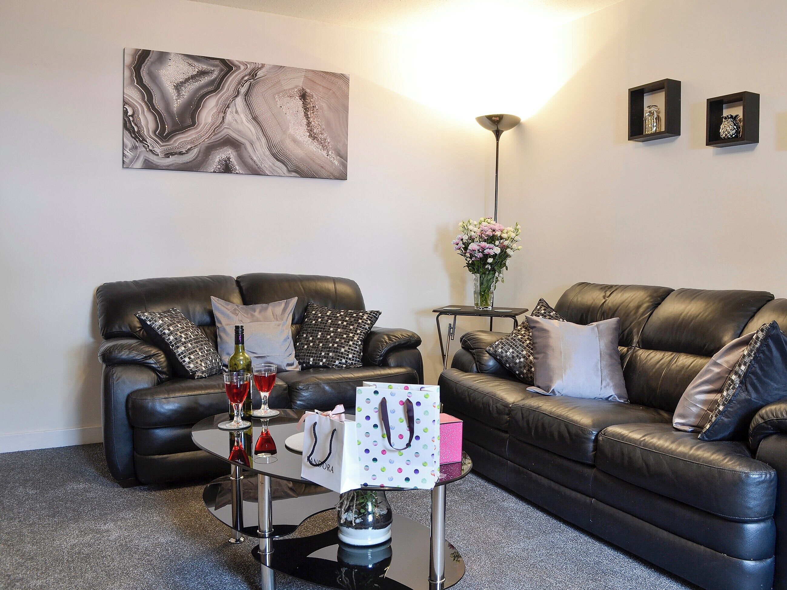 A modern living room with two black leather sofas, a glass coffee table, and a marble artwork on the wall.