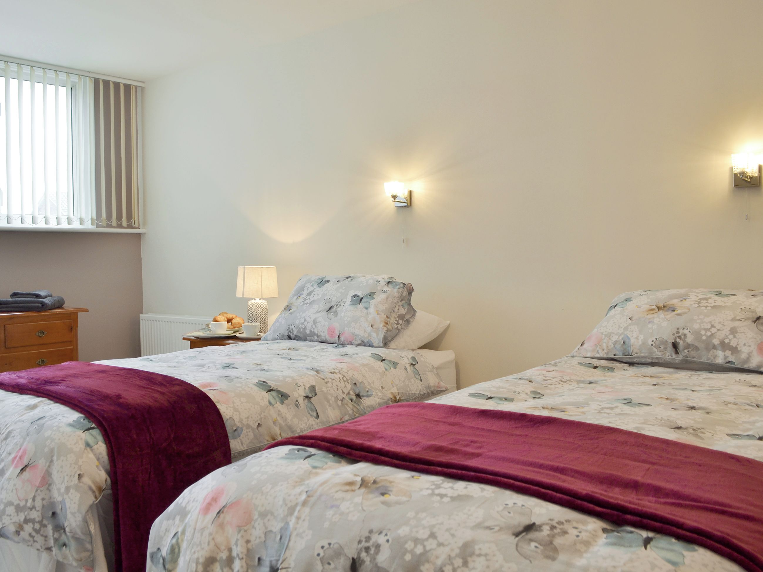 A bedroom with two beds, a nightstand, a lamp, and a window with blinds.