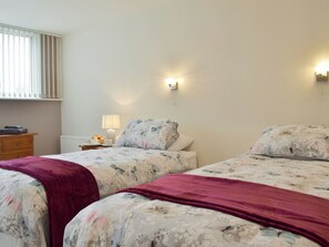 A bedroom with two beds, a nightstand, a lamp, and a window with blinds. - 2 bedroom accommodation in Whitstable (Whitstable)