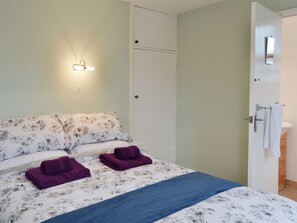 A bedroom with a bed, a nightstand, a wall-mounted light, a door, and a bathroom with a sink and mirror.
