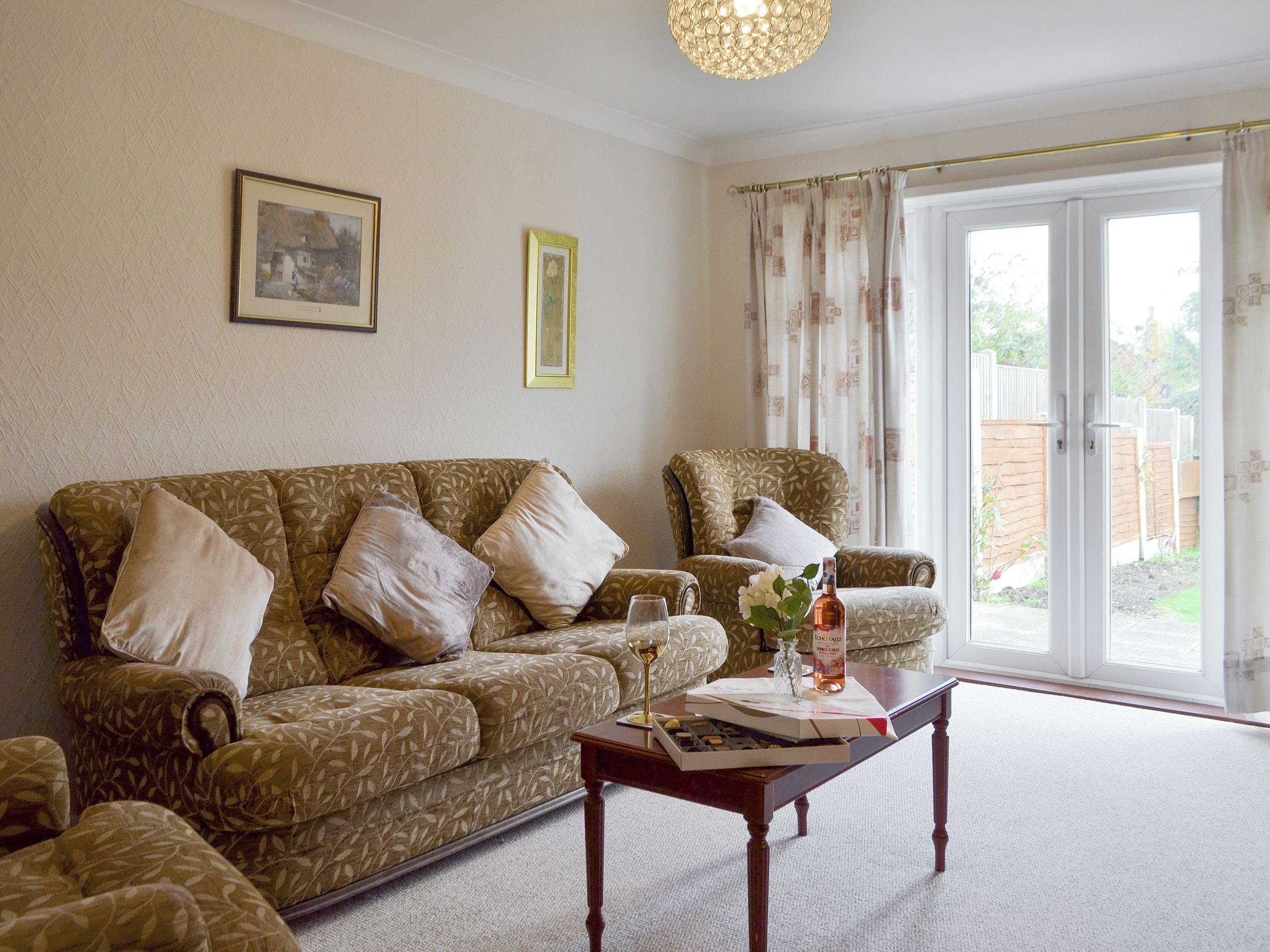 A living room with a patterned sofa, a matching armchair, a wooden coffee table, and a glass of wine.
