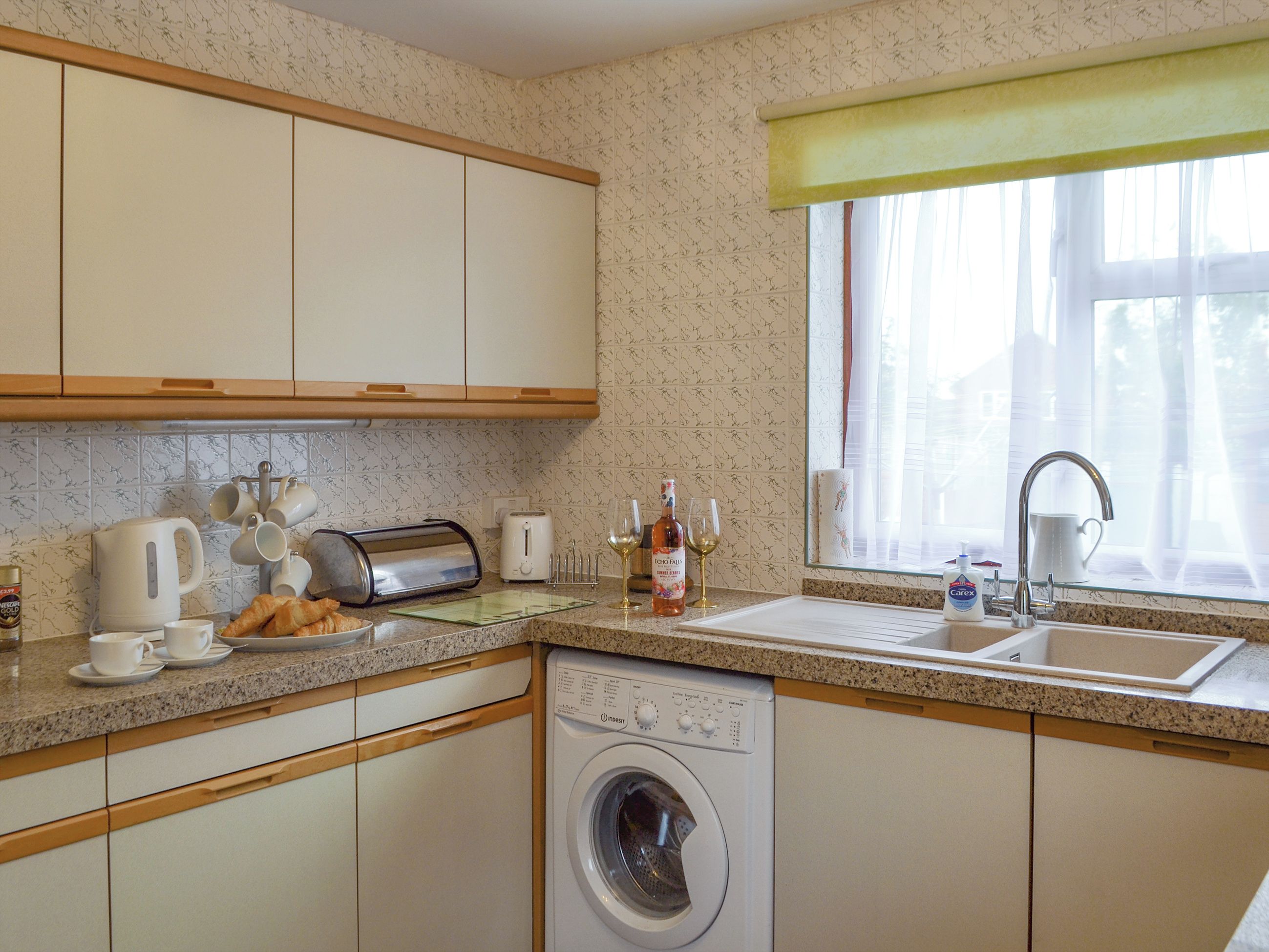 A kitchen with a washing machine, a sink, and a window with curtains.