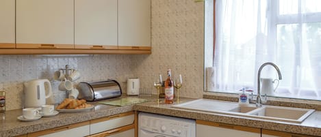 A kitchen with a washing machine, a sink, and a window with curtains.