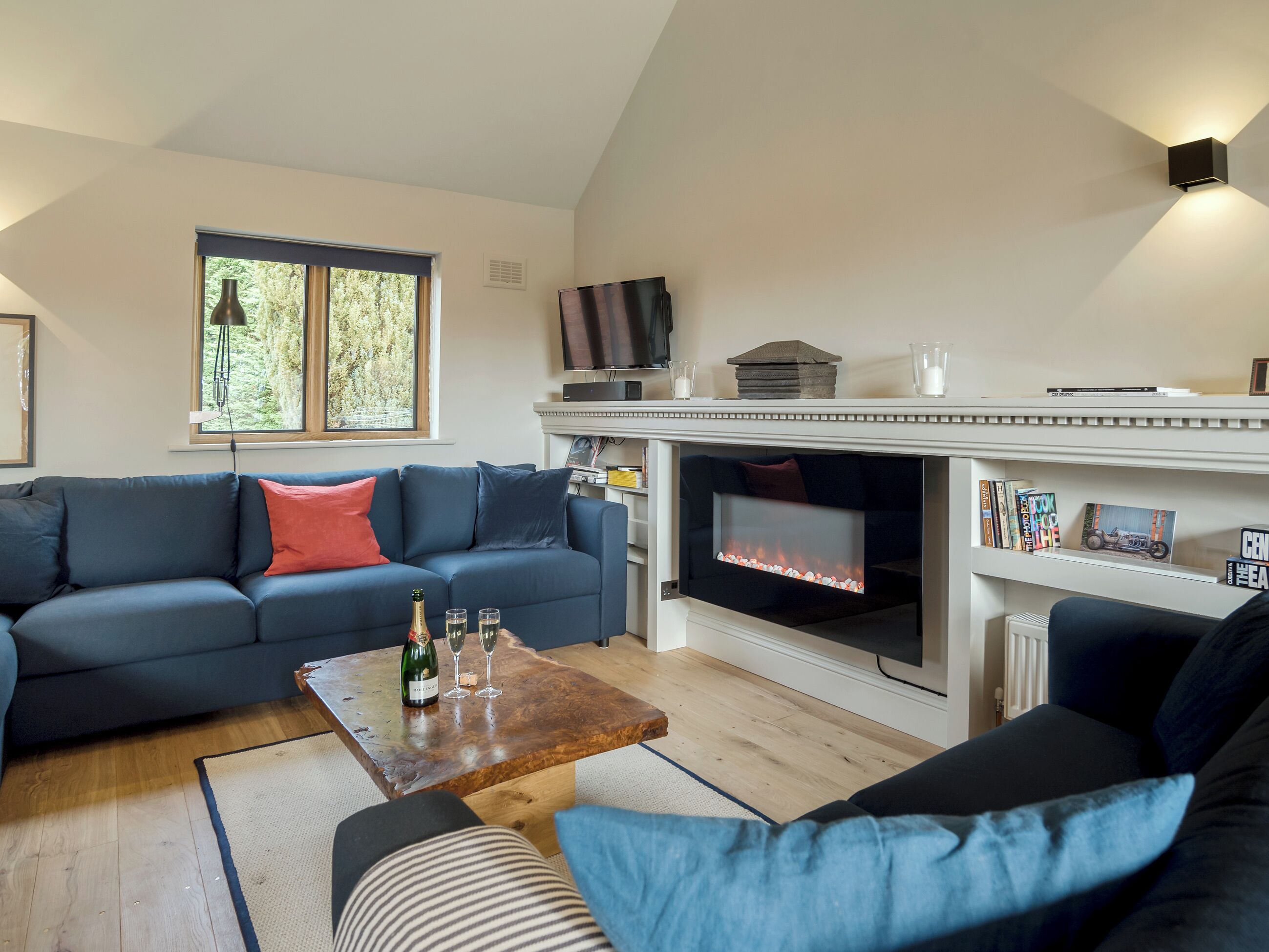 A living room with a fireplace, a sofa, a coffee table with drinks, and a television.