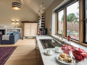 A modern kitchen with a large window, a dining area with a sofa, and a breakfast setup with biscuits and tea. - 3 bedroom accommodation in Stretton-on-Fosse, near Moreton-in-Marsh (Stretton-on-Fosse, near Moreton-in-Marsh)