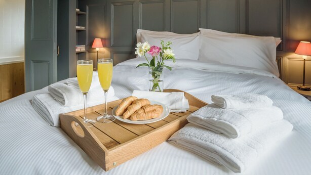 Ein ordentlich bezogenes Bett mit einem Tablett mit Frühstücksartikeln, darunter Croissants und Gläser Orangensaft.